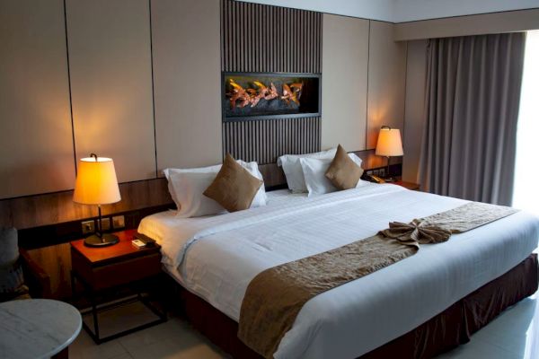A hotel room with a neatly made bed, two bedside tables with lamps, wall art above the headboard, and a window with curtains.