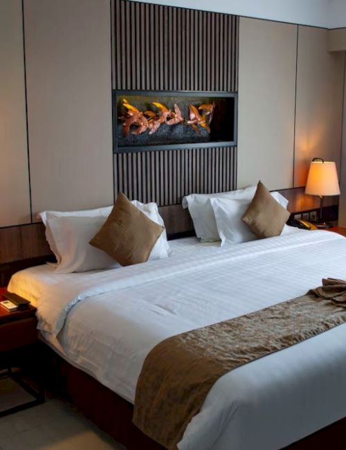 A cozy hotel room with a large bed, two side tables with lamps, decorative pillows, and a wall art piece, all illuminated with warm lighting.