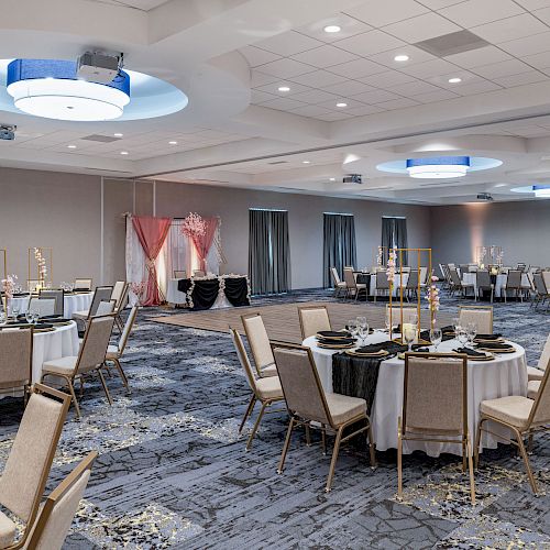 The image shows an elegant banquet hall with round tables set for an event, featuring pink drapes and decorative items.