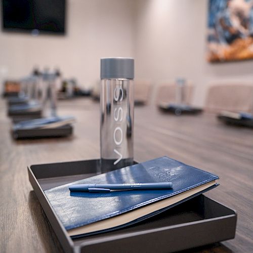 A conference room table setting with a bottle of water, a notebook, and a pen placed on each tray in front of the chairs.