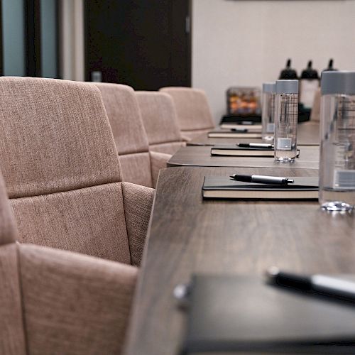 A conference room table with beige chairs, notebooks, pens, and bottled water arranged neatly, indicating preparations for a meeting.