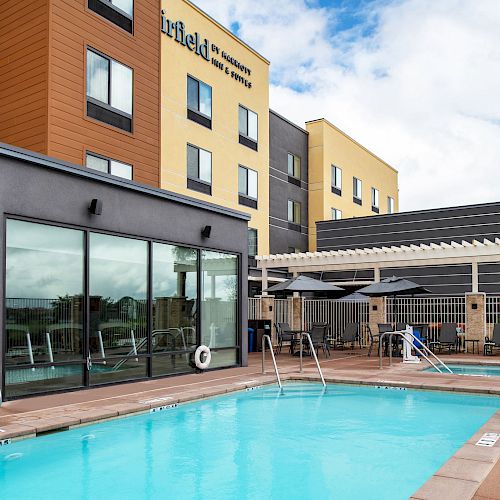 An outdoor pool area at a hotel, with sun loungers, umbrellas, and a building in the background.