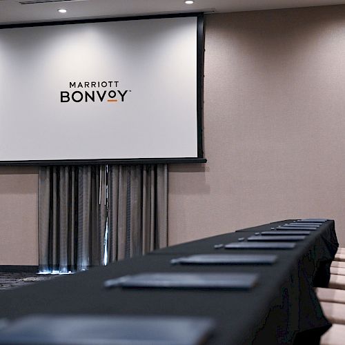 A conference room with a long table and chairs, facing a screen displaying 