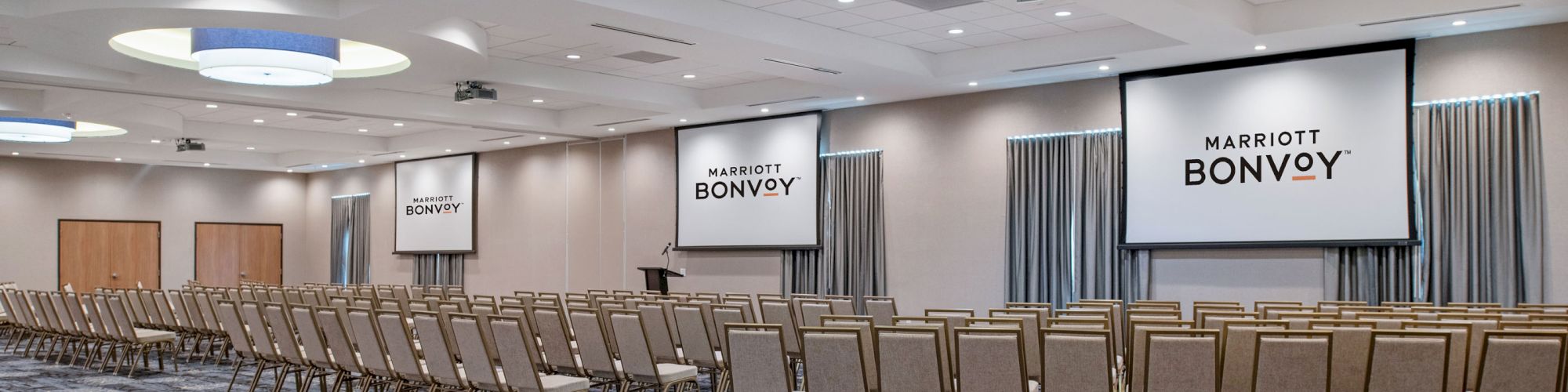 A conference room set up with rows of chairs facing two large screens displaying 