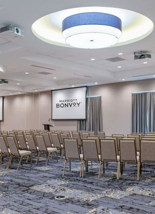 A spacious conference room with rows of chairs facing two large screens that display 