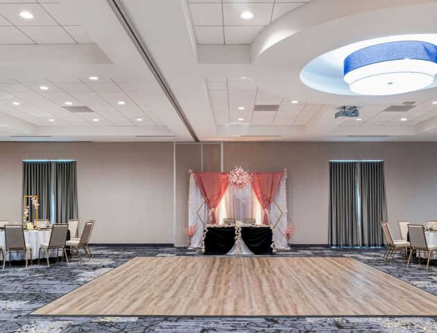 A decorated ballroom or event space with a dance floor, tables, and chairs arranged around the room, and an elegant setup under a canopy.