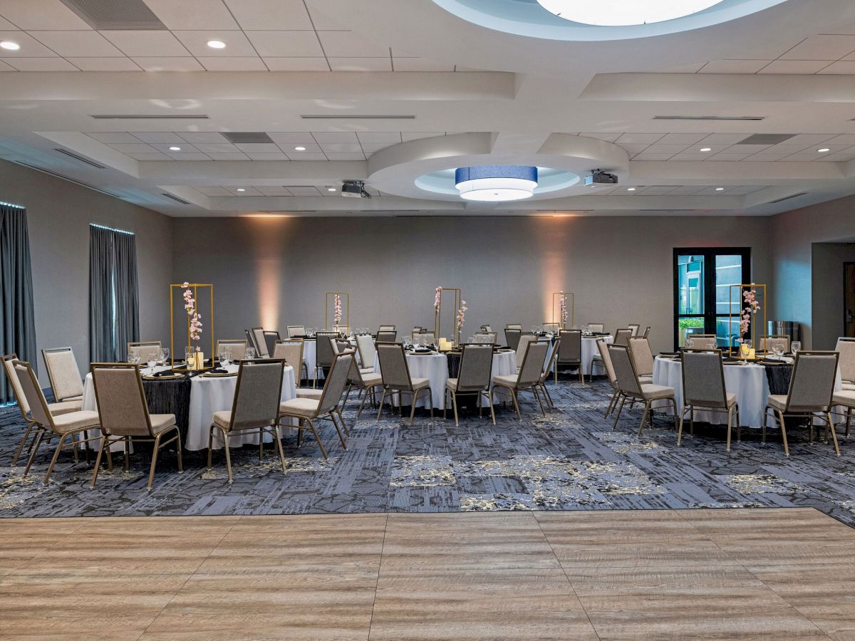 This image shows an empty, well-lit banquet hall with round tables and chairs neatly arranged, decorated with centerpieces on each table.