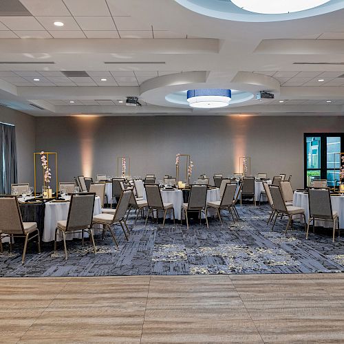 A modern, well-lit conference room with multiple round tables and chairs set up, ready for an event or meeting.