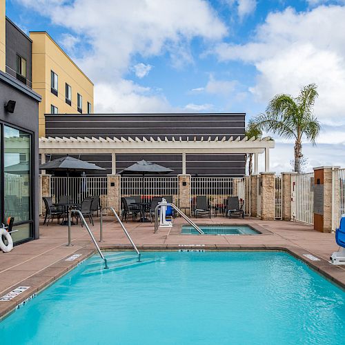 The image shows an outdoor hotel pool area with lounge chairs, a hot tub, and a pergola-covered seating area in the background.