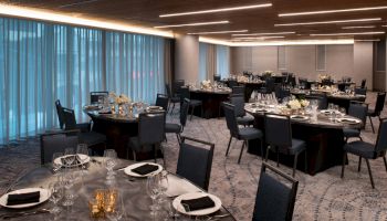 The image shows a well-decorated banquet hall with round tables set for an event, each adorned with black napkins, glassware, and floral centerpieces.