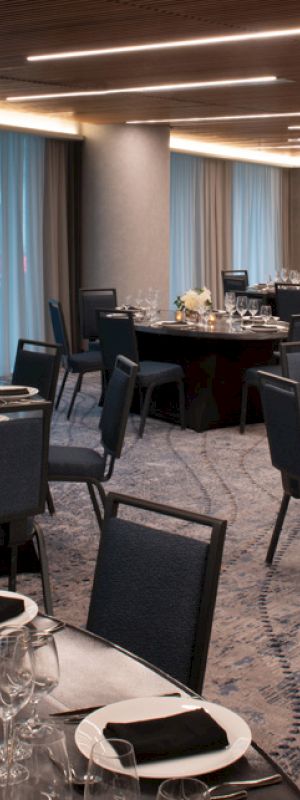 A formal dining room set for an event with round tables, black chairs, white table settings, and dim lighting.