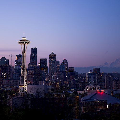This image features the skyline of Seattle at dusk, with the iconic Space Needle prominently visible and Mount Rainier in the background.