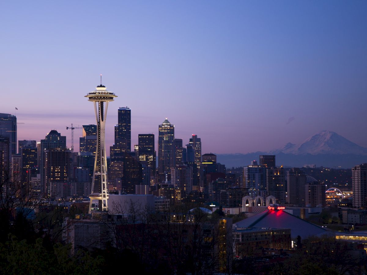 A twilight skyline of Seattle with the iconic Space Needle, city buildings, and Mount Rainier visible in the background, creating a picturesque scene.