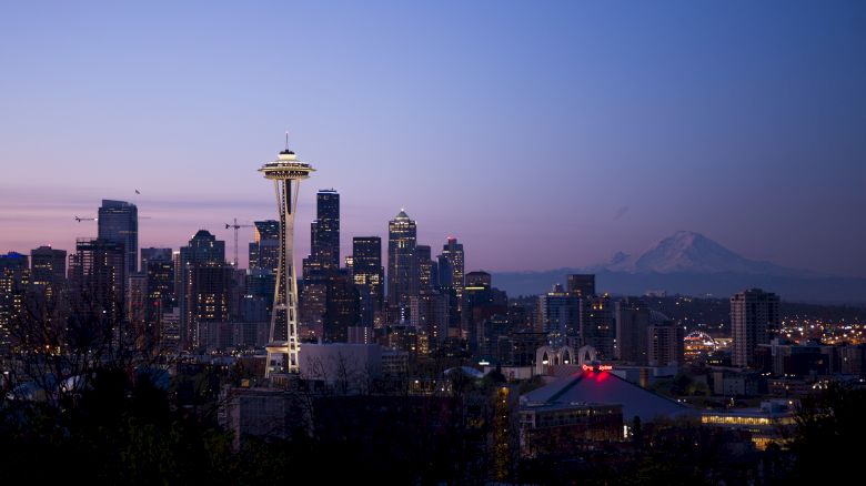 A twilight skyline of Seattle with the iconic Space Needle, city buildings, and Mount Rainier visible in the background, creating a picturesque scene.